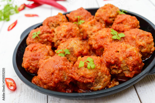 Meat balls in spicy tomato sauce served on a cast iron pan on a white wooden background. Close up