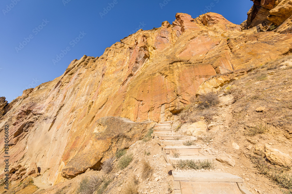 Fototapeta premium The steps for the tourists among the rocks. Unusual shaped rocks on the background of blue sky. Beautiful landscape of yellow sharp cliffs. Smith Rock state park, Oregon
