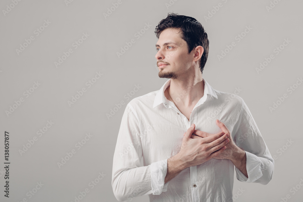 handsome young proud man in shirt holding hand on chest on grey handsome young proud man in shirt holding hand on chest on grey