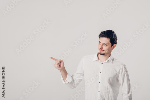 man with beard pointing copy space. young man in shirt pointing away on gray background. soft light