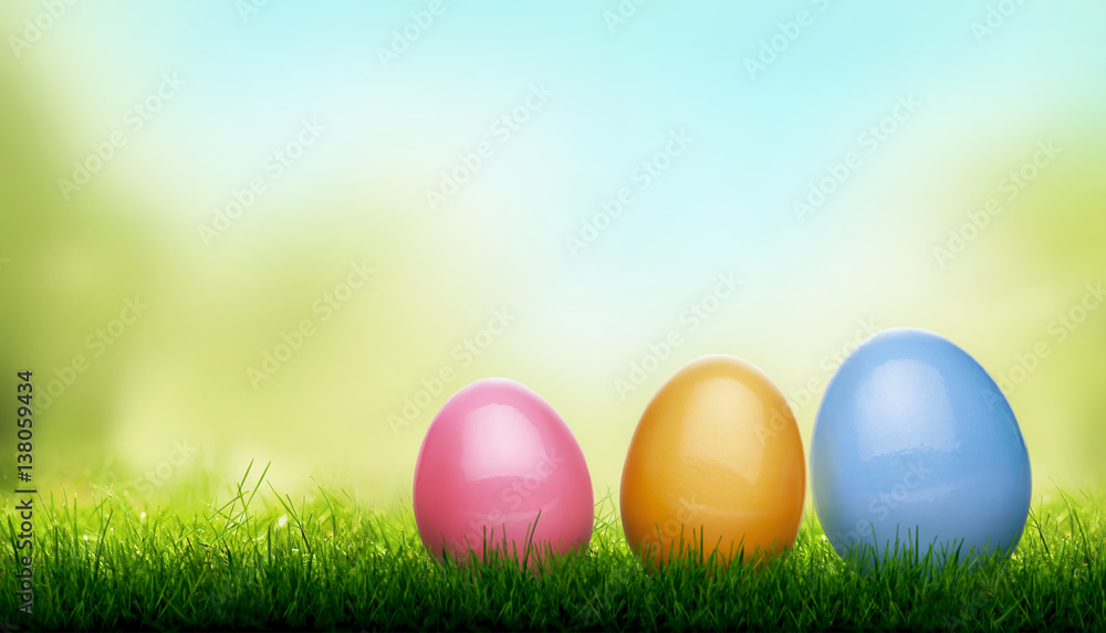 Decorated Easter Eggs, blades of Green Grass with a blurred bokeh sky blue and green garden foliage background.