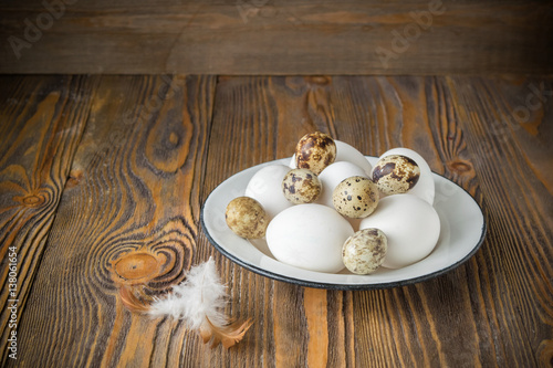 Fresh chicken and quail eggs a metal white plate on wooden dark background