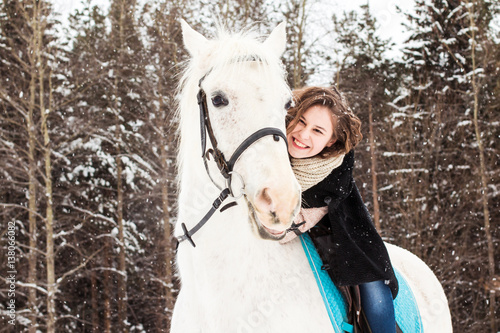 Nice girl and white horse outdoor in snowfall in a winter