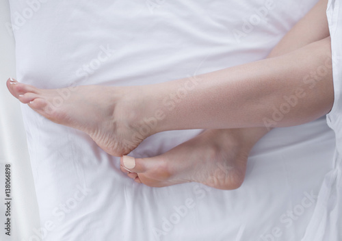 Close-up of soft female legs under bedcloth over white background