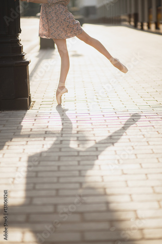 girl ballerina in Pointe shoes with a beautiful figure standing near a pillar in a pink dress, falls the shadow, the sun is shining, the asphalt pavement