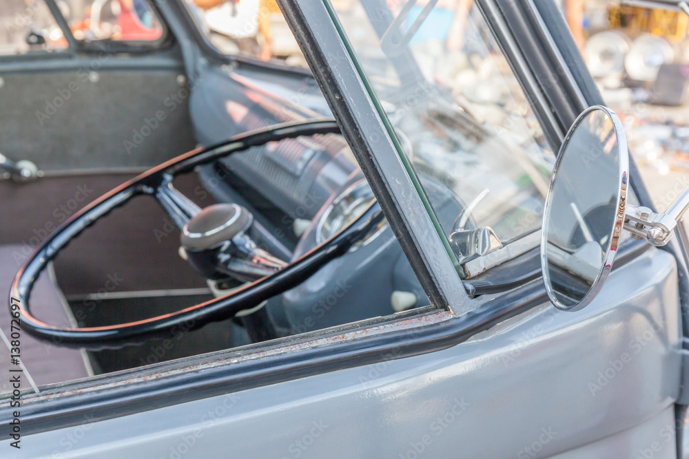 Shiny retro wing mirror of classic beetle grey and blurred background of steering wheel inside.