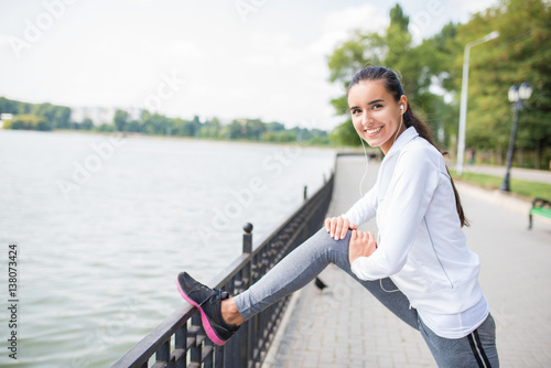 Healthy athlete girl stretching in park on sunny day. Sporty brunette female woman exercise outdoors. Fit woman doing marathon training. Fitness and motivation