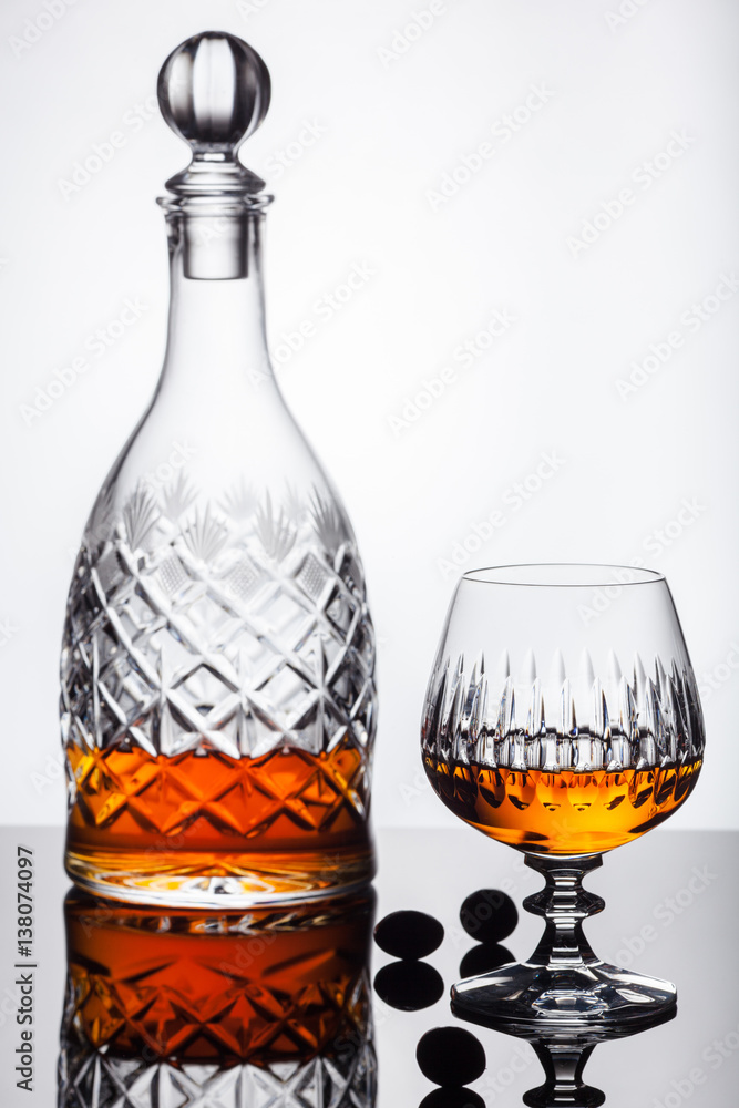 Crystal decanter and glasses with rum, carafe with whiskey on a glass table, white background Crystal decanter and glasses with rum, carafe with whiskey on a glass table, white background