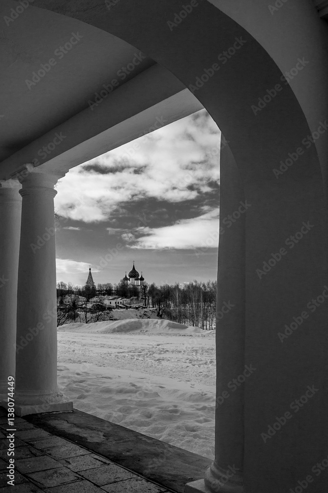 The view of the Orthodox Church through the arch. Black-and-white photograph of the Christian Church. The natural frame of the arch. Winter in Suzdal. Russia.