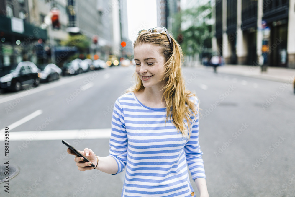 USA, New York, Manhattan, Young woman walking in the street, holding mobile phone