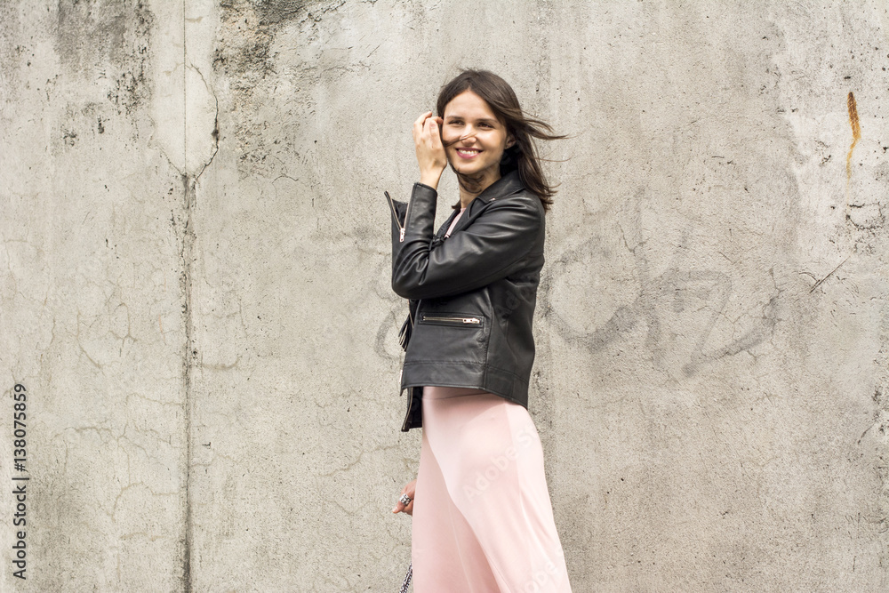 Portrait of smiling young woman wearing black leather jacket and pink dress in front of concrete wall Portrait of smiling young woman wearing black leather jacket and pink dress in front of concrete wall