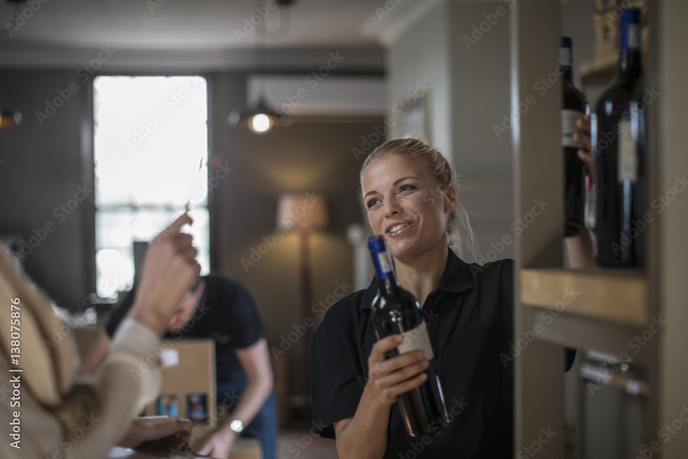 Smiling saleswoman packing wine bottles on shelf in wine shop Smiling saleswoman packing wine bottles on shelf in wine shop