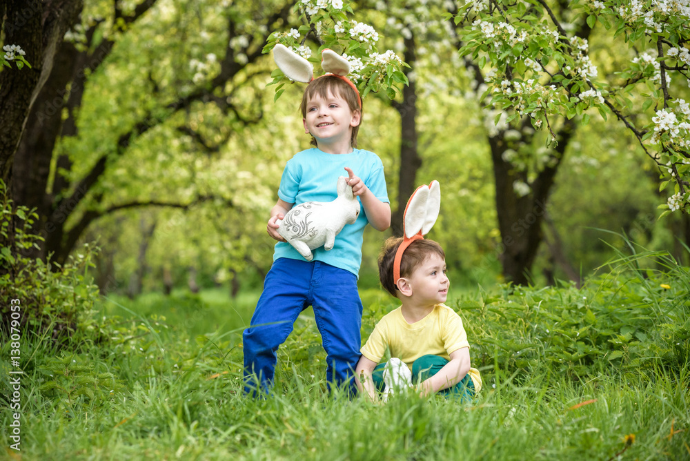 Two little kids boys and friends in Easter bunny ears during traditional egg hunt in spring garden, outdoors. Siblings having fun with finding colorful eggs. Old christian catholoc tradition Two little kids boys and friends in Easter bunny ears during traditional egg hunt in spring garden, outdoors. Siblings having fun with finding colorful eggs. Old christian catholoc tradition