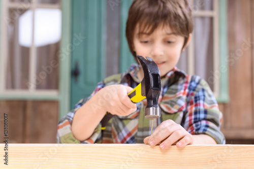 Close-up view of smiling boy hammering nail in wooden plank