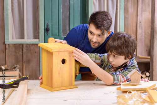 Concentrated father and son making wooden birdhouse together in workshop Fototapeta