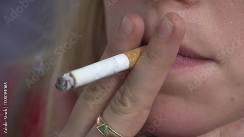 Young blond woman's lips with a lit cigarette, smoking in slow-motion. Cancer. 