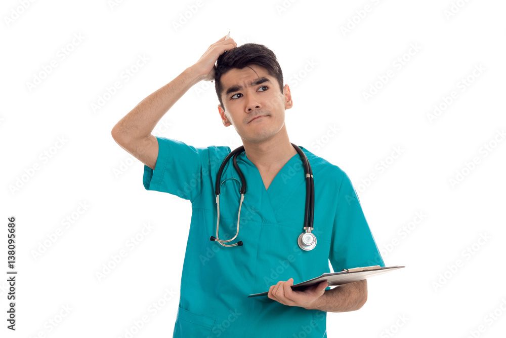 young funny brunette man doctor in blue uniform with stethoscope on his shoulders make notes and thinking isolated on white background young funny brunette man doctor in blue uniform with stethoscope on his shoulders make notes and thinking isolated on white background
