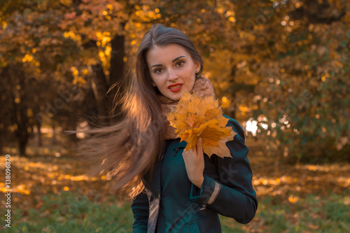 young girl stands in the Park and holds autumn leaves in hand
