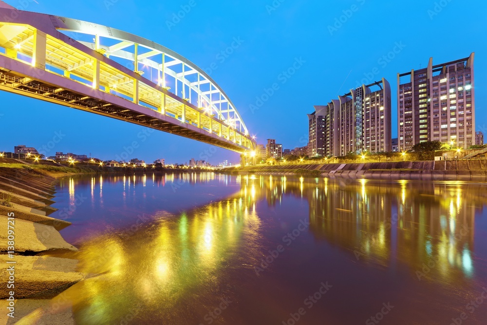 Naklejka premium Riverside buildings and the famous HuanDong Rainbow Bridge over Keelung River at dusk in Taipei Taiwan, Asia ~ A romantic landmark of Taipei, the Rainbow Bridge in evening twilight ( low angle view )