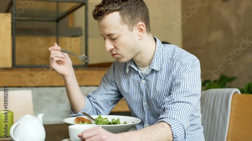 Young man eating lunch in the cafe and feeling unwell, steadycam shot
