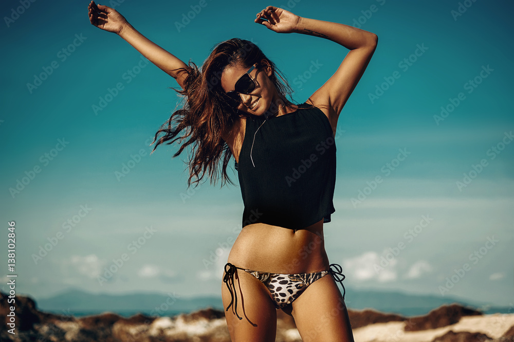 Fototapeta premium Piękna partyjna dziewczyna tanczy i macha ręki na plaży nad niebieskim niebem