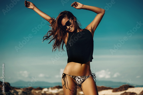 Beautiful party girl dancing and waving hands on the beach over blue sky