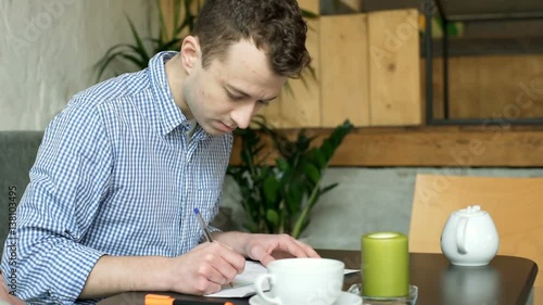 Young man sitting in the cafe after classes and doing homework, stedycam shot
 photo