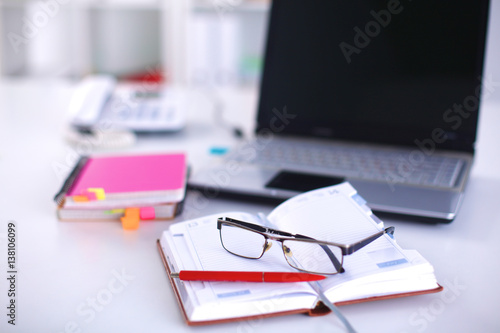 A note book, laptop, pen, graph paper document on the office desk table behind white blind