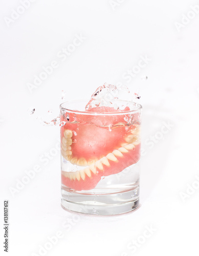 Two acrylic dentures immersed in a glass of water,white background.