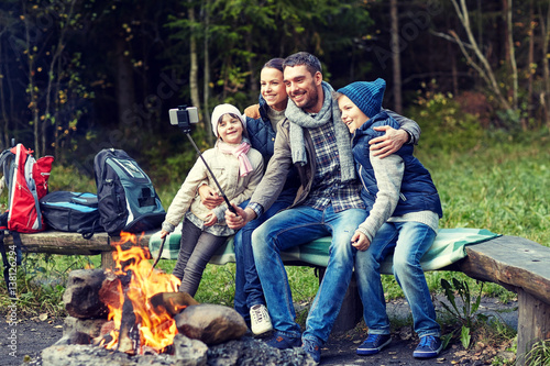family with smartphone taking selfie near campfire