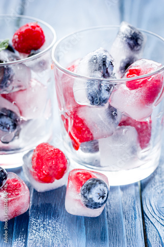 glass with frozen berries in cubes on wooden desk background