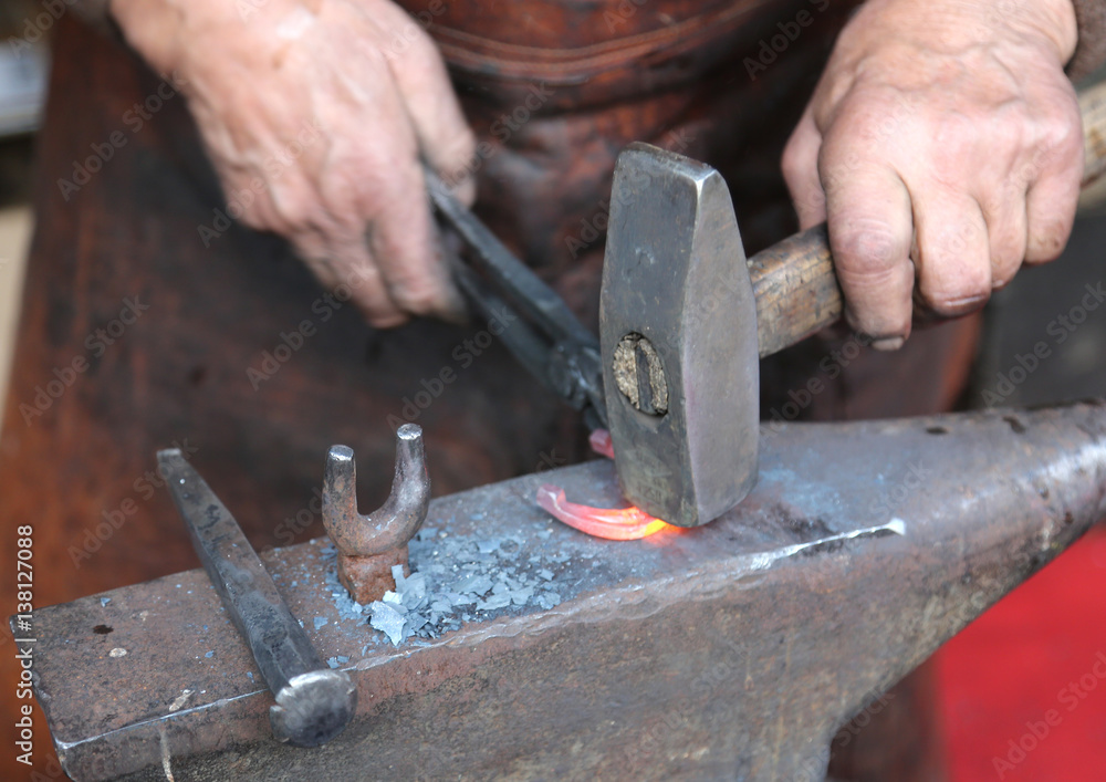 hands of an elderly blacksmith working iron with a hammer and th hands of an elderly blacksmith working iron with a hammer and th