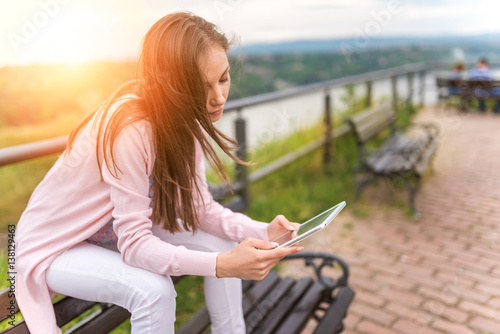 Beautiful young woman using tablet computer on a bench in park 