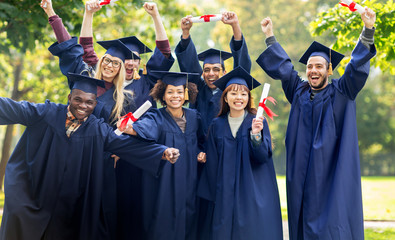 happy students in mortar boards with diplomas