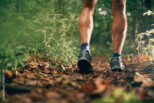 Muscular calves of a fit male jogger training for cross country forest trail race in nature park.