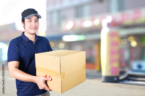 Asian Delivery man with cardboard box on blurred background.