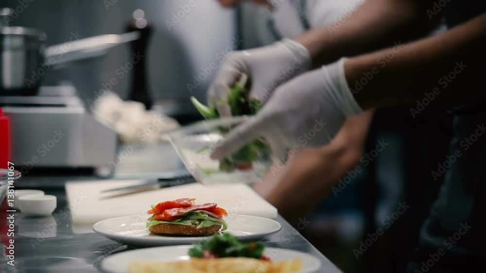 A man puts a salad next to a bun with fish. A man puts a salad next to a bun with fish.