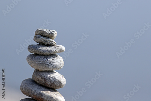 Column of hand piled granite rocks against blue water background