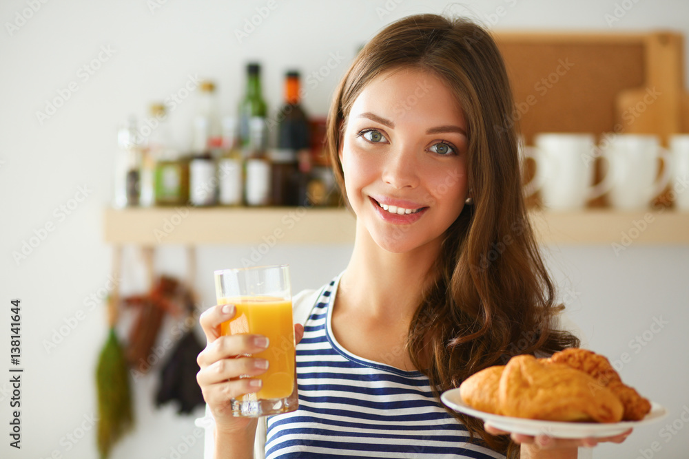 Young woman with glass of juice and cakes standing in kitchen Young woman with glass of juice and cakes standing in kitchen