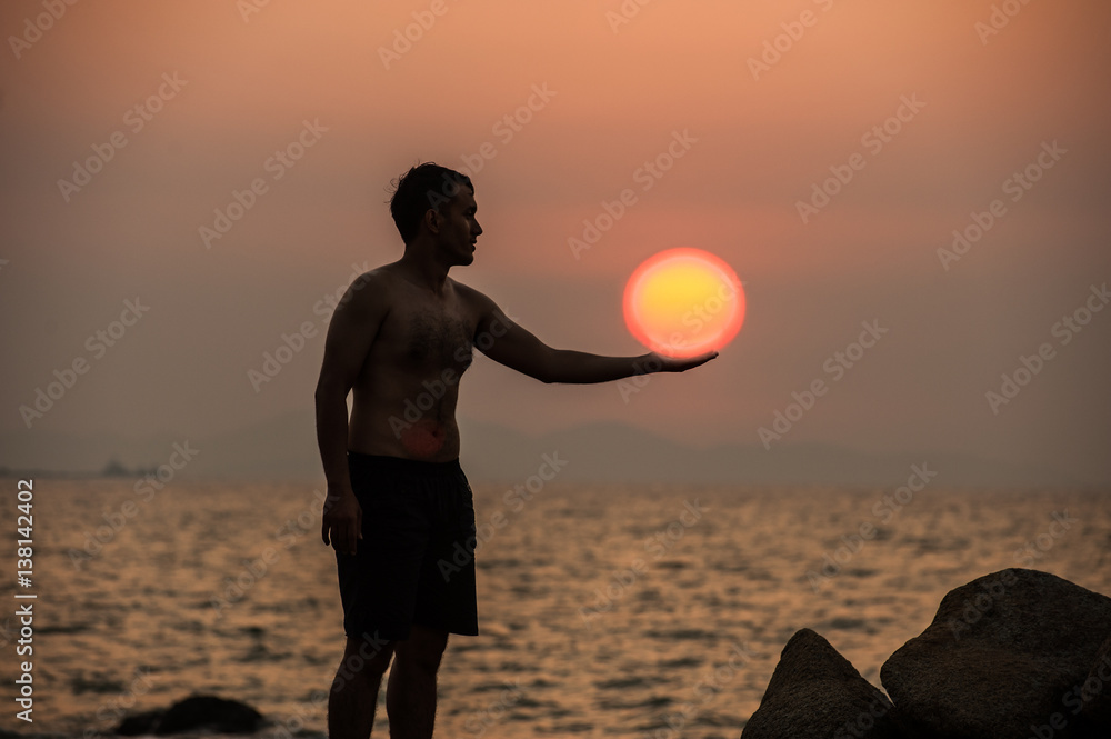 Male is engaged in fitness yoga exercise holding the Sun on the stone in Sunset.