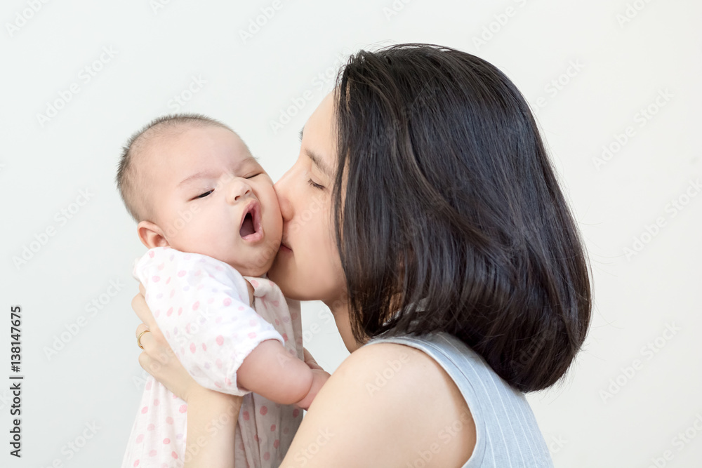 Portrait of happy asian mother kissing and hugging her cute little baby on grey background Portrait of happy asian mother kissing and hugging her cute little baby on grey background