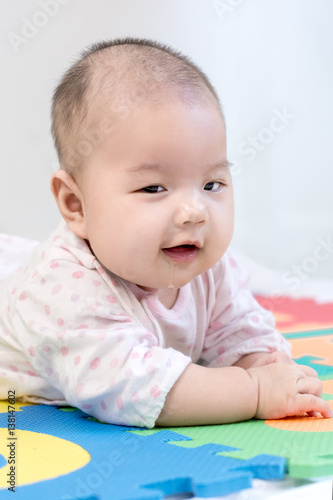 Portrait of a little adorable newborn infant baby girl with saliva lying on the tummy on colorful eva foam and looking in camera indoors