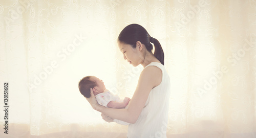 Happy Asian mother with her little cute newborn baby 0-1 month at home near window. loving mom holding adorable child baby sleeping in mother arms. Asian baby boy in the comfort of moms arms