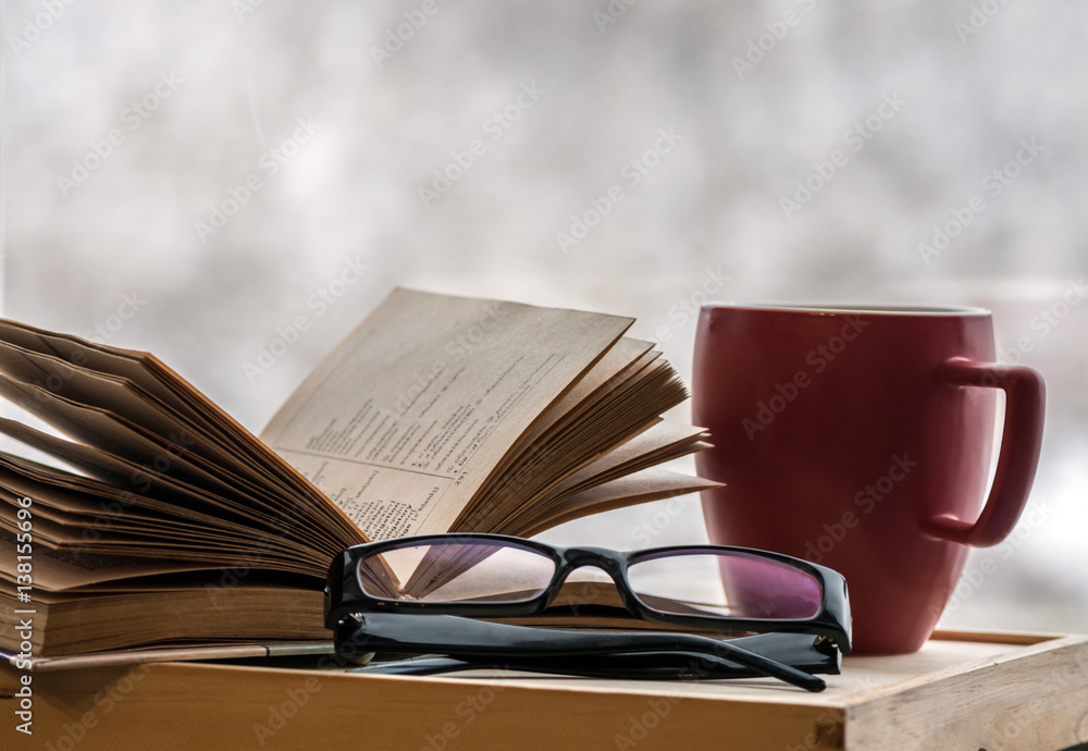 Reading an old book with glasses at home on a cold winter evening. Reading a book at home with coffee Reading an old book with glasses at home on a cold winter evening. Reading a book at home with coffee