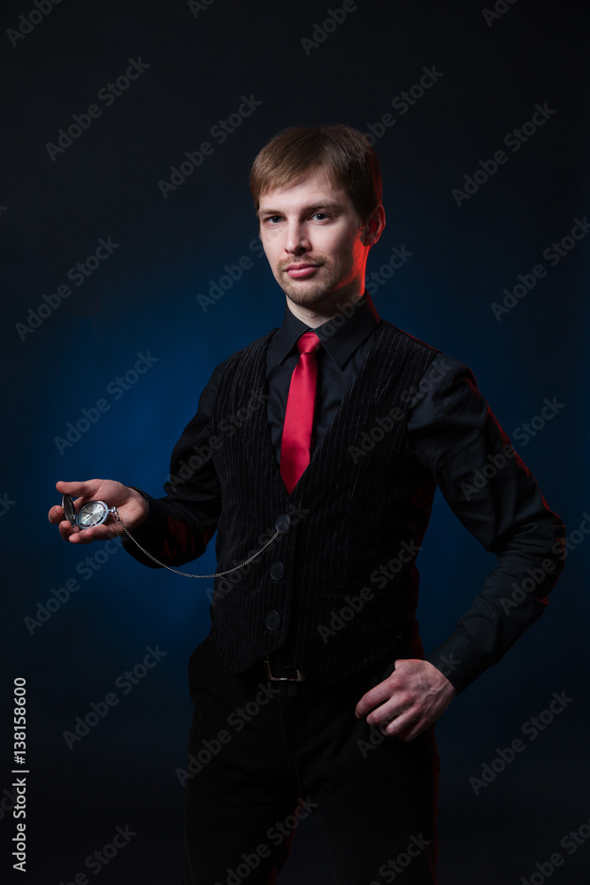 Intellegent solid man in black shirt and velvet vest with red tie holding a  pocket watch in his hand. Mysterious hypnotist standing on blue-black  studio background Stock Photo | Adobe Stock