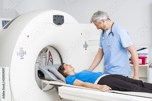 Smiling Doctor Talking To Patient Lying On CT Scan Machine