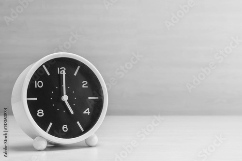 Closeup alarm clock for decorate in 5 o'clock on wood desk and wall textured background in black and white tone with copy space