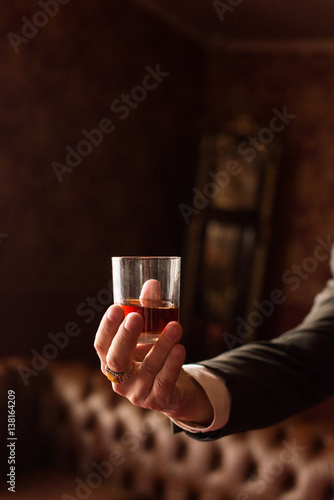 Groom holds in his hand a glass of whiskey indoors