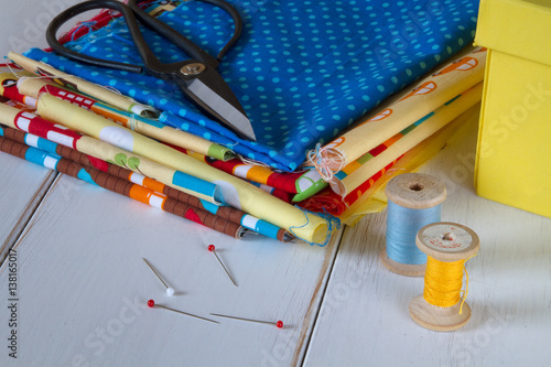 Colorful fabrics with vintage scissors, pins, measuring tape and cotton threads on white wooden table photo