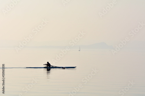 A man with his canoe paddling on the lake; backlit photo, sillhouette.